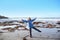 Positive woman in a warm jacket spread her arms and legs on the seashore during low tide in winter