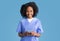 Positive young african american curly lady nurse in blue uniform typing, chatting on smartphone