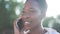 Positive young African American woman talking on phone smiling standing in sunlight outdoors. Close-up portrait of happy