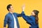 Positive young couple give high five, agree to work as team, stand sideways,  on yellow wall. Male student with notepad
