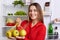 Positive young female with glad expression comes from grocer`s shop with new purchase, shows fresh apples, going to put them in fr