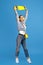 Positive young woman hold over head yellow penny or skateboard over blue background.