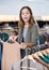 Positive young woman holding beige jumper on a rack while searching for clothes in a showroom