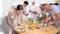 Positive young woman in striped apron participating in group cooking class, standing at table and seasoning prepared