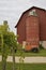 A post covered with grape vines is in front of an old truck parked by a silo and hip roofed red barn.