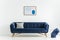 Poster above blue sofa with cushion in white living room interior with blanket in basket. Real photo