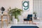 Poster above blue wooden armchair in flat interior with plant next to table and lamp. Real photo