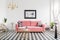 Poster above pink settee in spacious living room interior with plants and gold armchair. Real photo