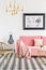 Poster above pink sofa with blanket in living room interior with gold chair and table. Real photo