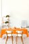 Poster on cabinet in white and orange dining room interior with wooden chairs at table