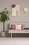 Poster and clock above couch in grey and pink living room interior with plant. Real photo