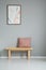 Poster on grey wall above wooden bench with pink pillow in simple apartment interior. Real photo