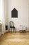 Poster on white wall above chair and cabinet in simple flat interior with wooden floor. Real photo