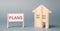 A poster with the word Plans and a miniature wooden house. Property investment. Estate planning. Living trust. Rental housing. Tax