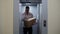 Postman deliveryman talks on phone with customer, holds cardboard box and getting out of the elevator