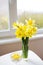 Posy of bright yellow daffodils on white wooden table.
