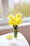 Posy of bright yellow daffodils on white wooden table.