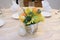 A pot of artificial flowers set up as decoration on a dinning table with light colored beige table cloth