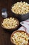 A pot of fresh popped popcorn and two bowls on a rustic wood table with salt shaker. Vertical format