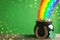 Pot with gold coins, horseshoe and clover leaves on wooden table against green background, space for text. St. Patrick`s Day