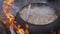 A pot of soup cooked over a fire. Stir soup with soup ladle, which is cooked in a cast iron over a fire. food in a big kettle