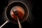 Pot and spoon with beef stock while cooking a red wine morel sauce on a black stove, dark background with copy space, high angle