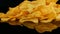 Potato chips lie on a mirror surface randomly scattered on a black background. Harmful food, fast food rotating