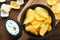 Potato corrugatedchips. Fast food. Crispy potato chips ceramic black bowl with sour cream sauce and onions in wooden stand on old