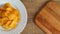 Potato grooved chips on a white plate and a cutting board with free space