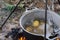 Potatoes are cooked in boiling water in a cauldron over a fire in the camp at sunset