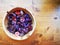 Potpourri of violet, purple and pink flowers and barks inside bamboo bowl on rustic wooden table.