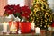 Potted poinsettias, burning candles and festive decor on wooden table in room. Christmas traditional flower
