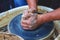 The potter forms a future product from a piece of clay on a potter`s wheel. Potter`s hands at work_