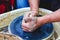 The potter forms a future product from a piece of clay on a potter`s wheel. Potter`s hands at work_