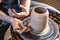 Potter working on a Potter`s wheel making a vase. Woman forming the clay with her hands creating jug in a workshop