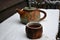 A pottery cup of steaming black tea and a teapot in the falling snow