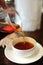 Pour freshly brewed black tea from a glass jug into a ceramic tea bowl