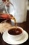 Pour freshly brewed black tea from a glass jug into a ceramic tea bowl