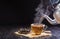 Pour a hot herbal teapot into a glass cup, teacup, and dry tea leaves in a wooden spoon and place it on a black wooden table