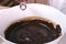 Pour and mix glycerin to liquid dark chocolate in a white bowl. Close-up view.