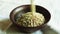 Pour raw green buckwheat into a plate. Fresh green buckwheat kernels fall into a clay brown bowl, close-up. Raw Healthy Organic Di