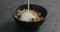 Pour yogurt over whole grain granola with hazelnuts and pumpkin seeds in black bowl on terrazzo countertop