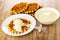 Poured condensed milk, transparent dipper on wafer in saucer, wafers, bowl with condensed milk on table