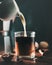 Poured milk into glass with black coffee drink, on wooden table at dark background