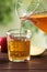 Pouring apple juice into glass on table against blurred green background