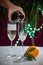 Pouring of brut champagne, cava or prosecco wine in glasses with garland lights on dark background, new year or birthday party