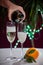 Pouring of brut champagne, cava or prosecco wine in glasses with garland lights on dark background, new year or birthday party