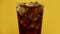 Pouring cola fizzy drink glass full of coke sparkling soda with ice cubes yellow