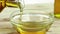 Pouring cooking olive oil in the bottle in the white container with drops on wood table background near olive oil bottle