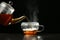 Pouring delicious hot tea into glass cup on table against dark